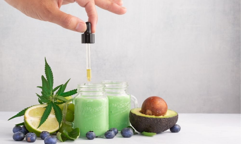 a hand using a dropper to put cbd oil in their green smoothie