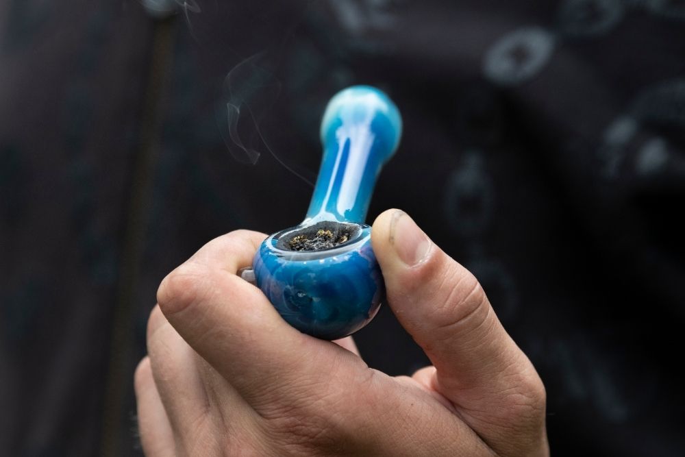 man smoking blue glass pipe