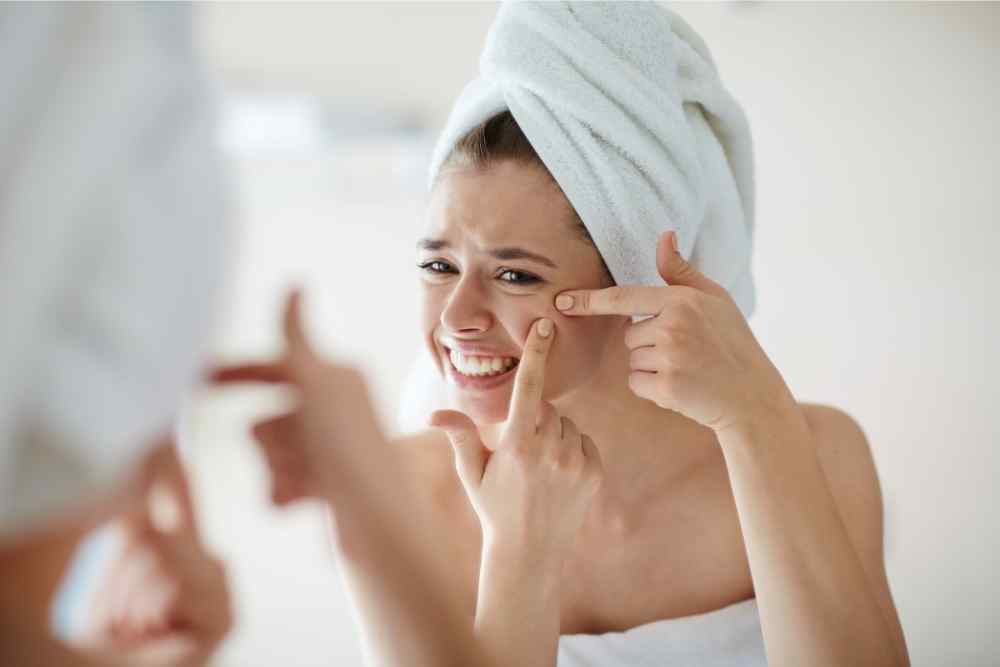 teen girl squeezing pimple in mirror